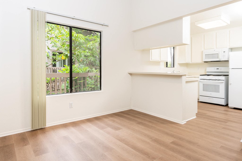an empty living room with a kitchen and a large window