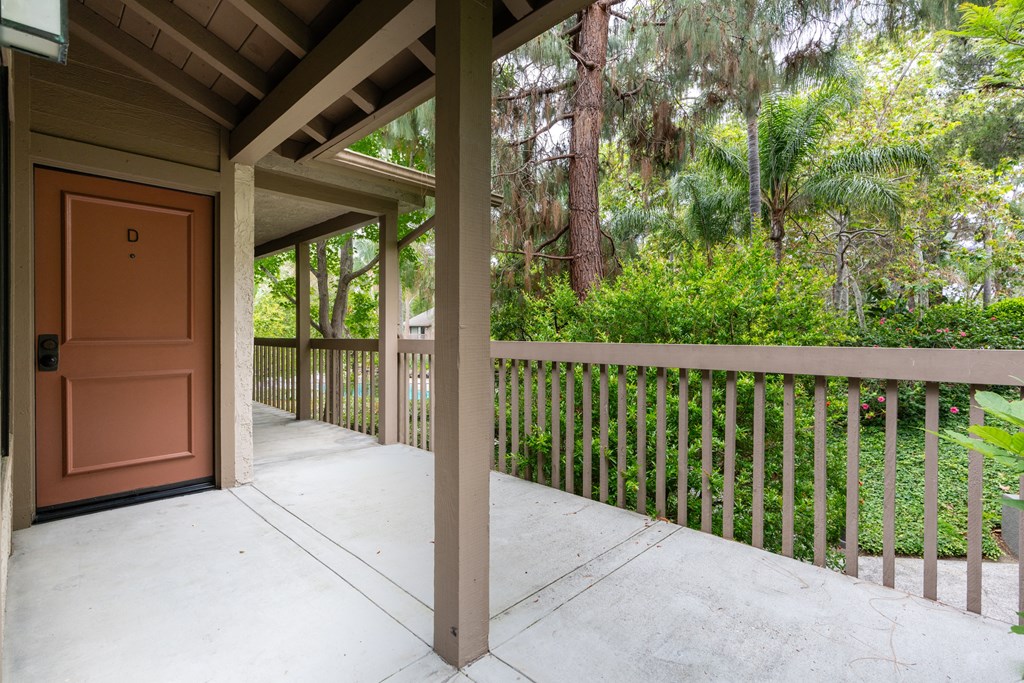 a covered porch with an orange door and a wooden railing