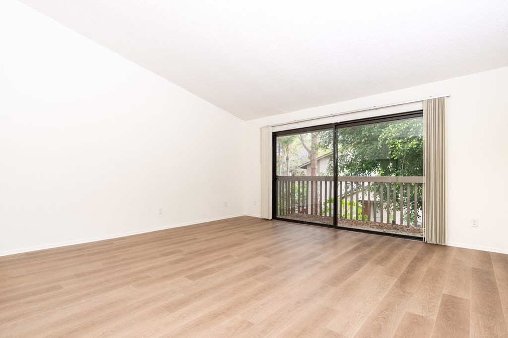 an empty living room with a sliding glass door to a balcony