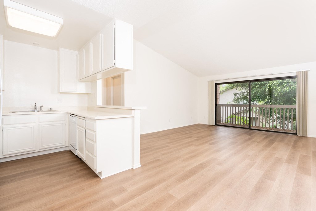 an empty living room with a kitchen and a balcony
