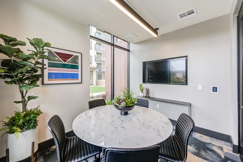 a round table with black chairs and a potted plant in the corner of a room with