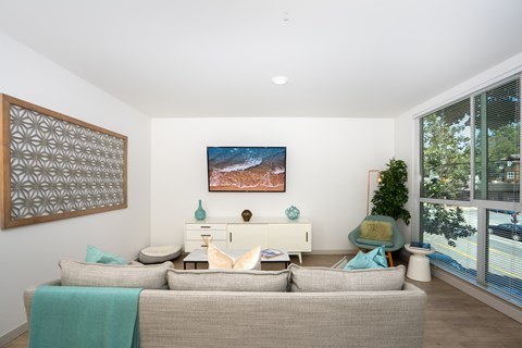 A living room with a grey couch and a painting on the wall.