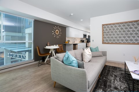 A living room with a grey couch, a white table, and a large window with a view of a building.