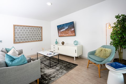 A living room with a grey couch, a white side table, a blue chair, and a painting on the wall.