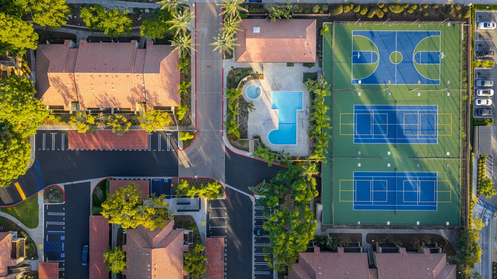 An aerial view of a tennis court and a swimming pool surrounded by buildings and trees.