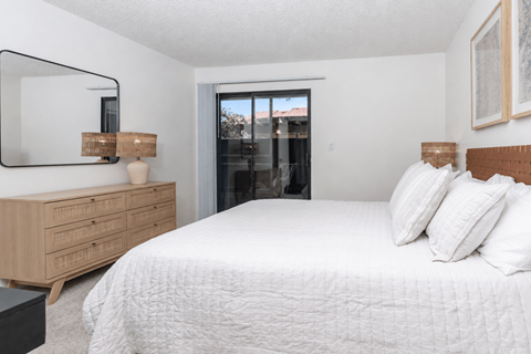 A bedroom with a large bed, a wooden dresser, and a mirror.