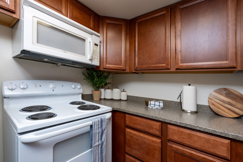 A white microwave oven mounted above a white gas stove in a kitchen with wooden cabinets.