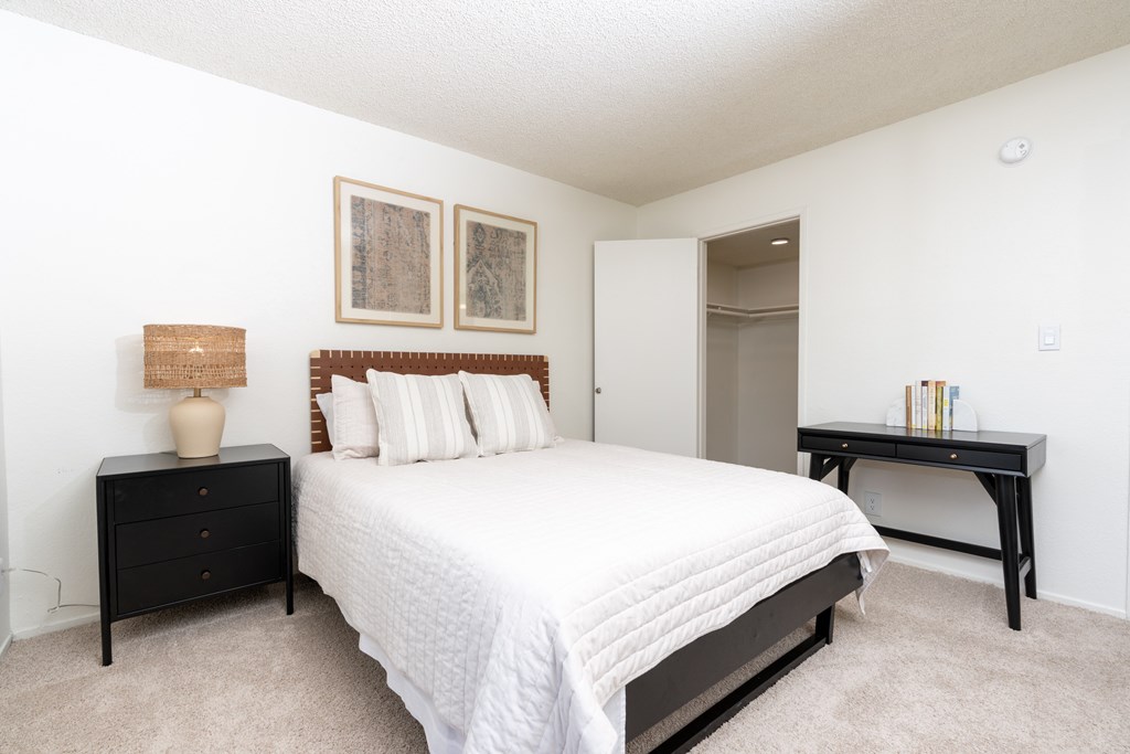 A bedroom with a bed, nightstand, and desk.