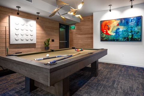 A pool table with a green plant and a painting on the wall.
