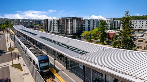 A train station with a train on the tracks and buildings in the background.