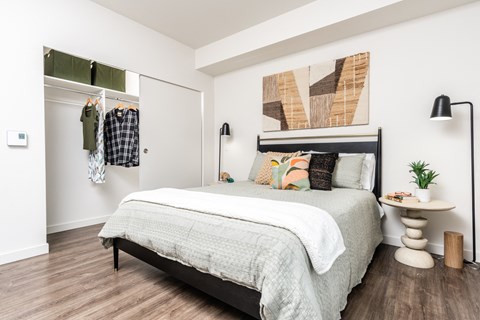 A bedroom with a bed, a clothing rack, and a painting on the wall.