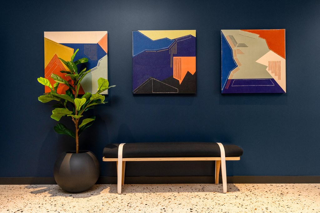 three paintings hanging on a blue wall with a bench and a plant