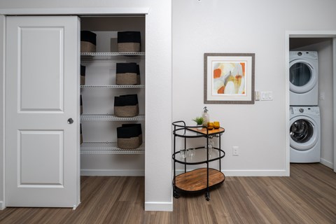 A laundry room with a washer and dryer, a shelf with baskets, and a cart with a bottle of dish soap.