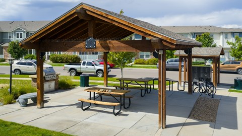 A wooden pavilion with picnic tables is surrounded by cars and houses.