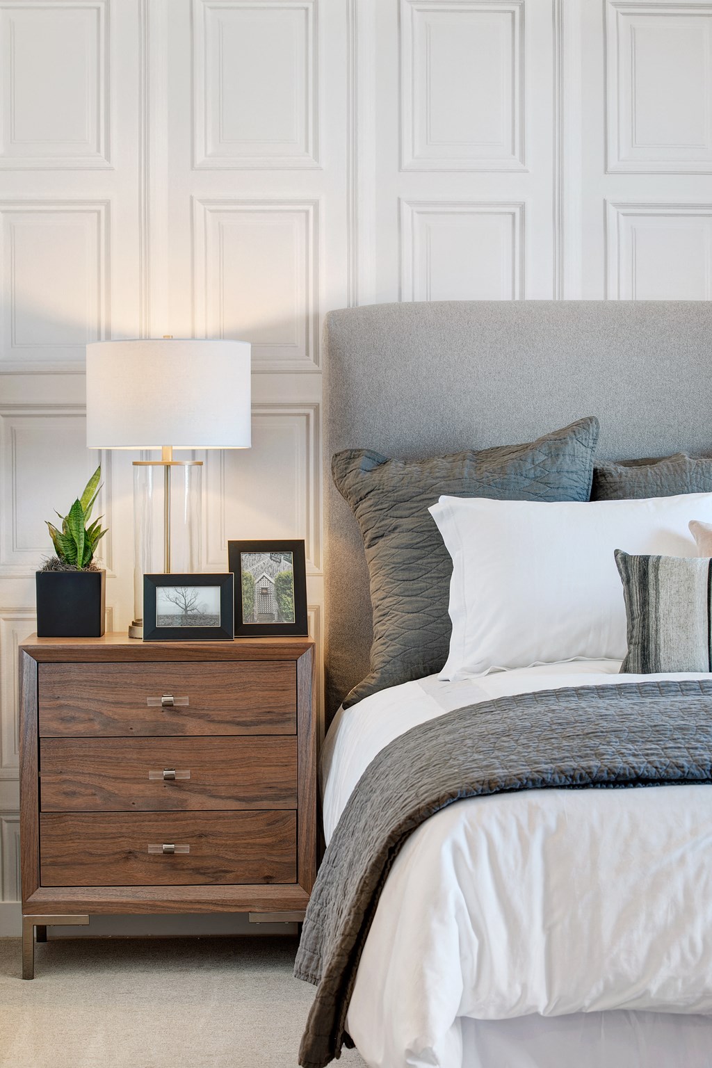 a bedroom with white walls and a bed with a gray headboard and pillows