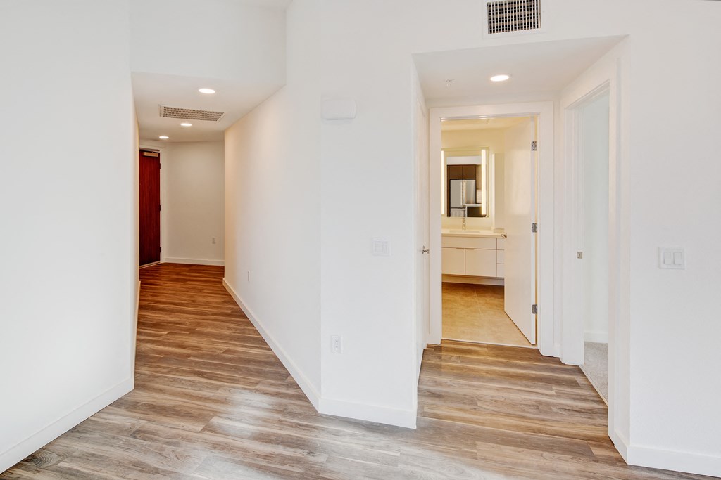 a corridor with white walls and wood floors and a white bathroom