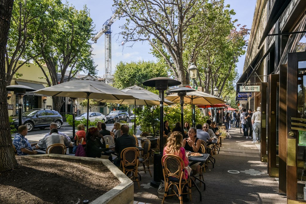 people sitting at tables on a sidewalk outside a restaurant