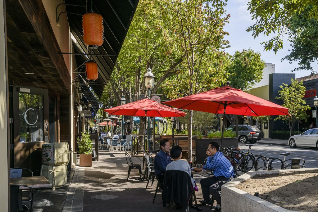 people sitting at tables under red umbrellas on a sidewalk