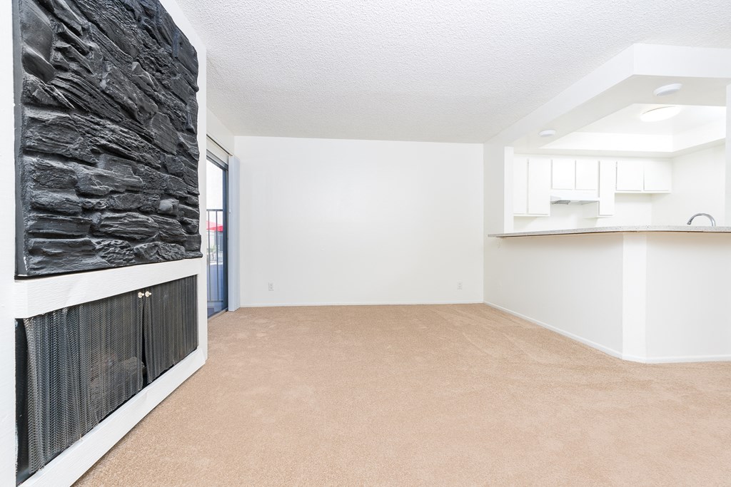 an empty living room with a fireplace and a kitchen