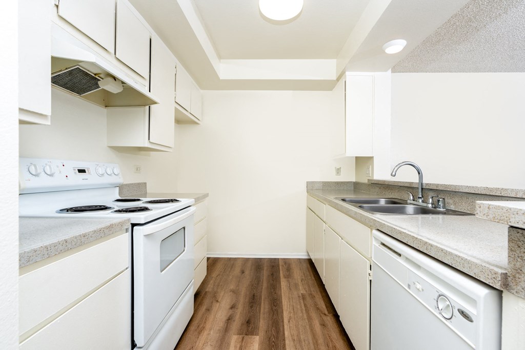 A white kitchen with a stove, sink, and cabinets.