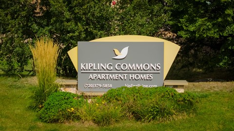 A sign for Kipling Commons Apartment Homes is displayed in front of some trees.