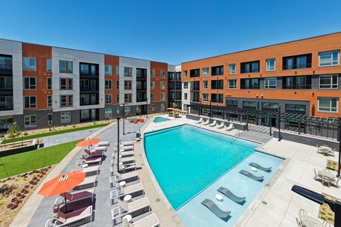A swimming pool surrounded by sun loungers and umbrellas in front of a building.
