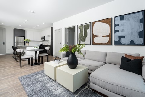 A modern living room with a grey sofa, a white coffee table, and a dining table with chairs.