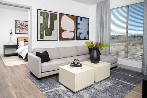 A living room with a grey couch, a coffee table, and three abstract paintings on the wall.