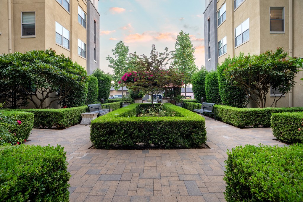 a courtyard with benches and hedges in front of an apartment building