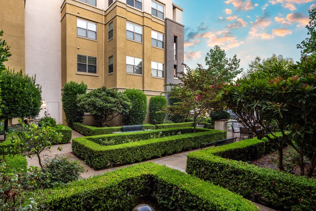 a garden with hedges and trees in front of a building