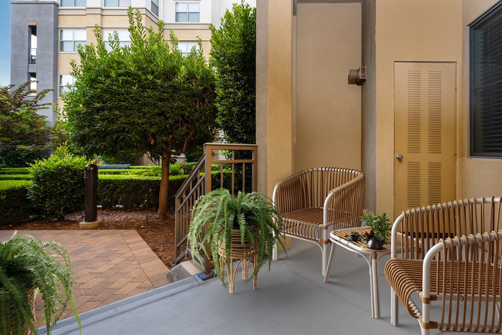 a patio with chairs and potted plants and a building in the background
