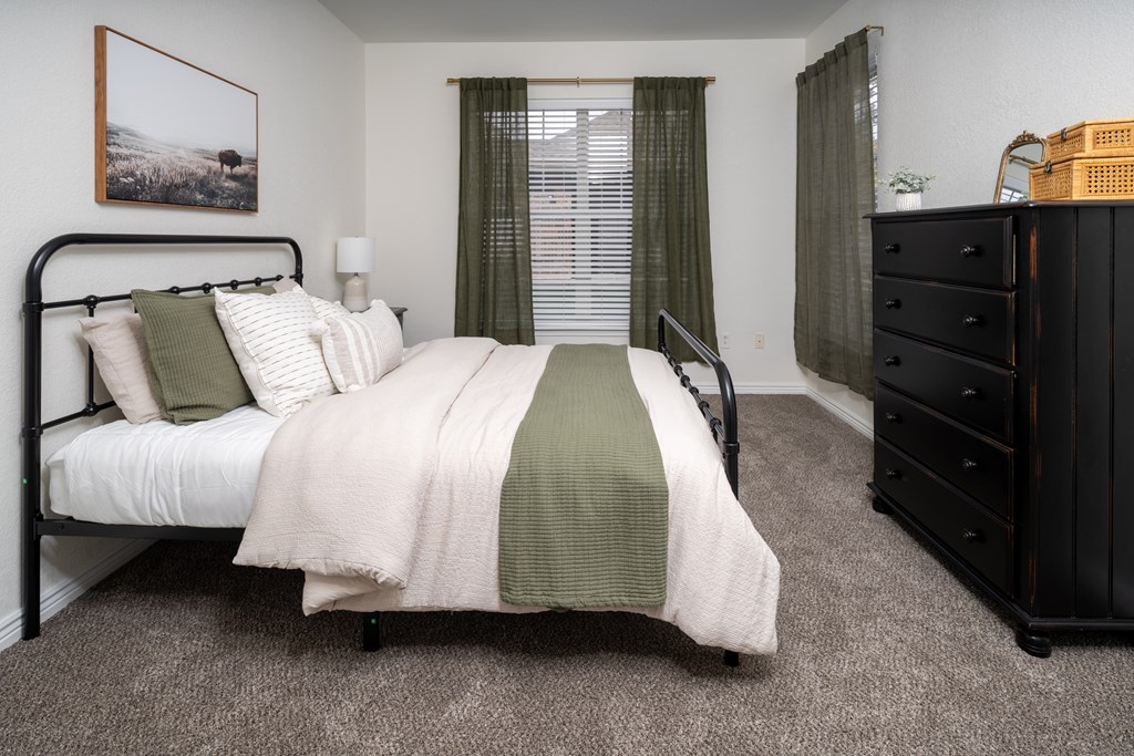 A bedroom with a bed, dresser, and window.