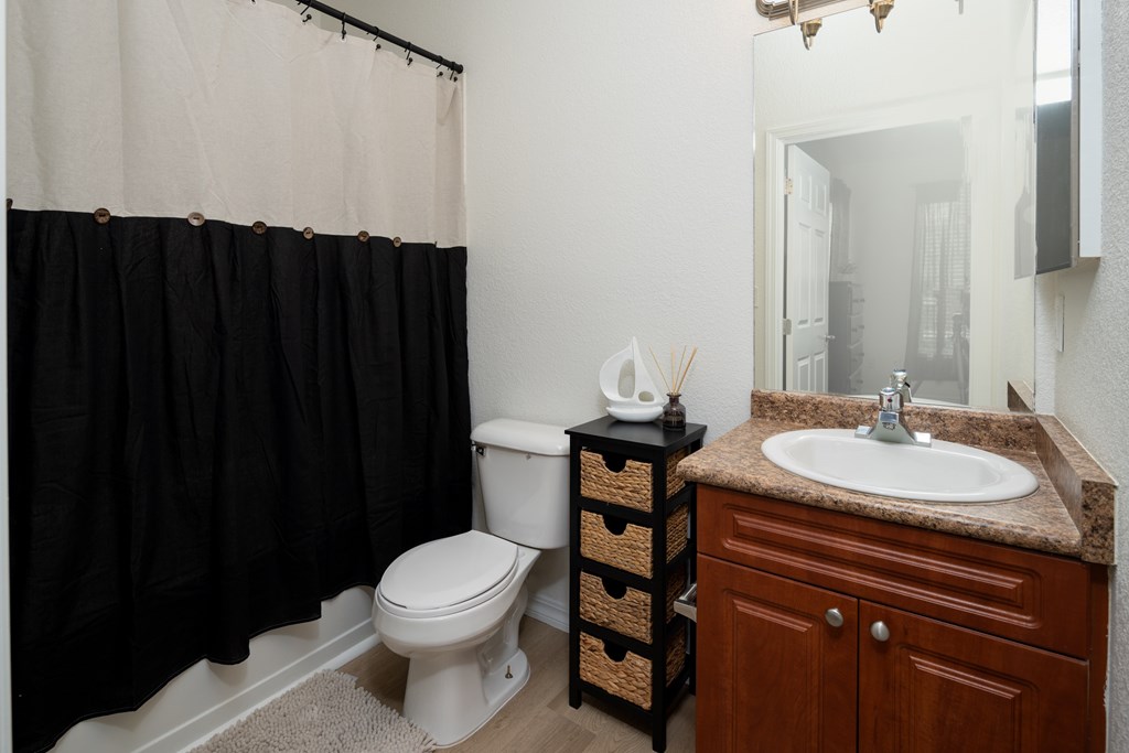 A bathroom with a white toilet, a brown cabinet, and a black shower curtain.