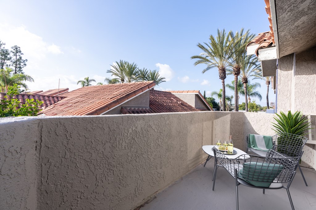 A patio with a table set for two and a view of a roof and palm trees.