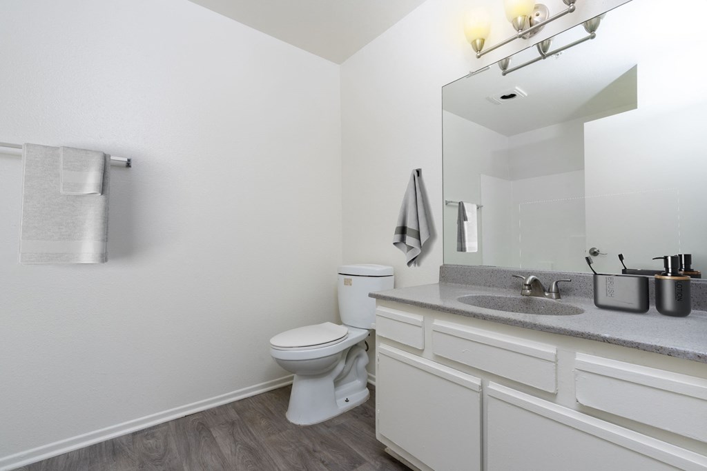 A white toilet sits in a bathroom with a white sink and a mirror above it.