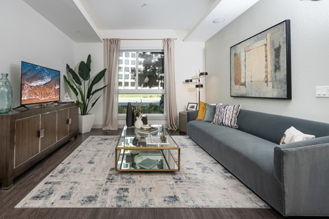 A modern living room with a grey sofa, a glass coffee table, and a large painting on the wall.