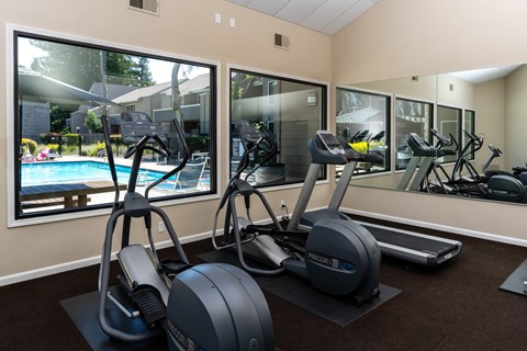 A gym with treadmills, elliptical machines, and a view of a pool.