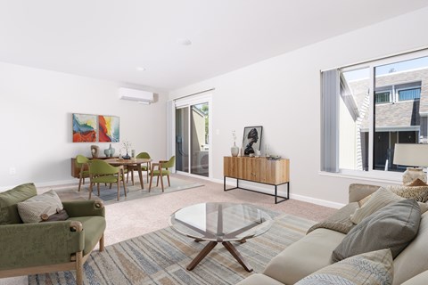 A living room with a green couch, a glass coffee table, and a wooden cabinet.