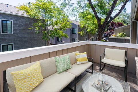 A patio with a couch, pillows, and a glass table.