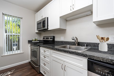 A kitchen with white cabinets and black countertops.