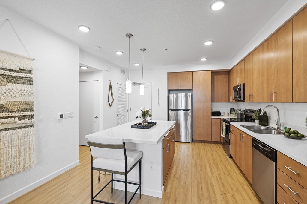 The Edge Milpitas CA a kitchen with wooden cabinetry and a large white island with a white countertop