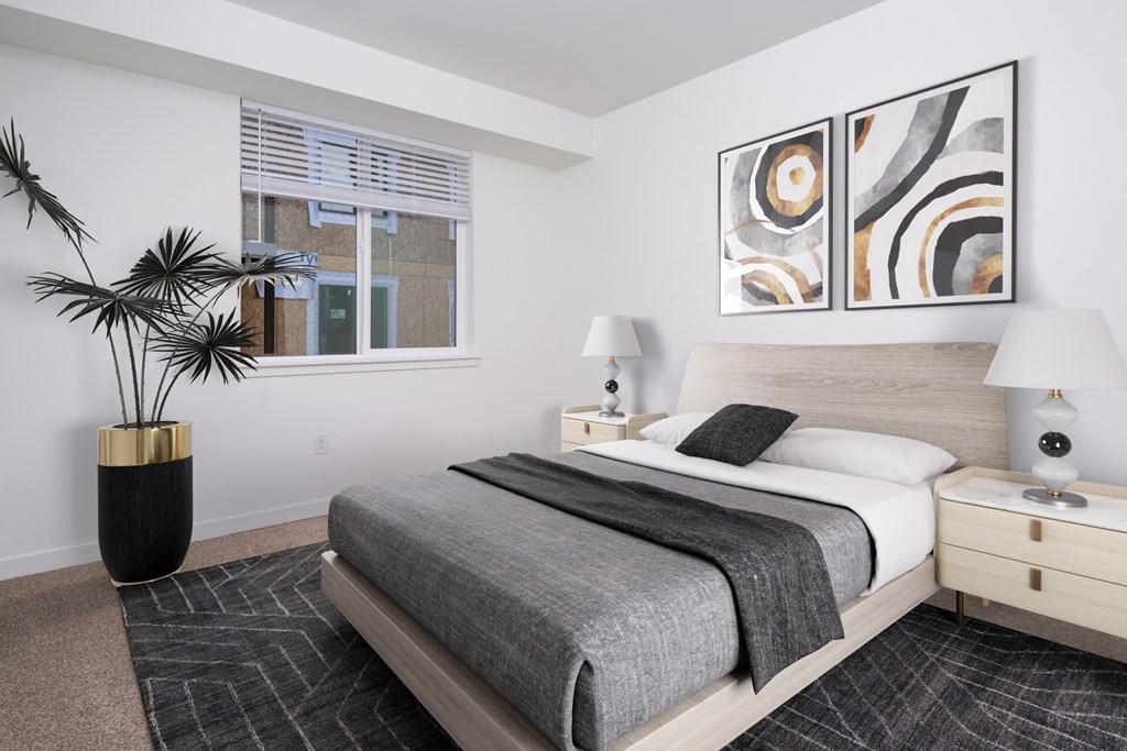 A bedroom with a bed, nightstand, lamp, and a plant.