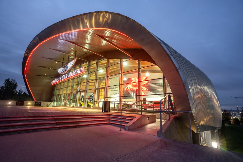A modern building with a curved roof and glass windows is illuminated at night.