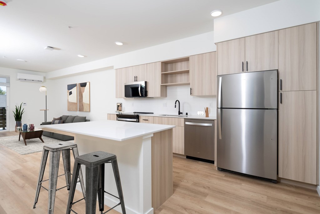 A modern kitchen with a refrigerator, bar stools, and a dining area.