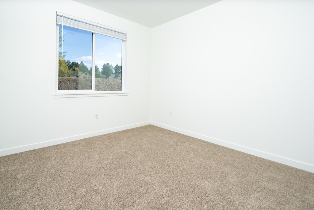 A room with a carpeted floor and a window showing a view of trees and sky.