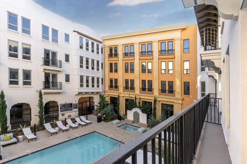 A pool is surrounded by lounge chairs in a courtyard.