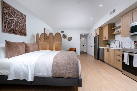 A bedroom with a large bed and a kitchen area in the background.