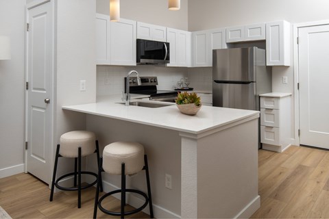 A kitchen with white cabinets and a white island with two stools.