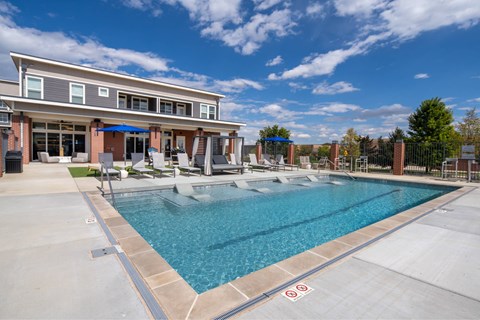 A swimming pool in front of a building with a blue sky and clouds in the background.