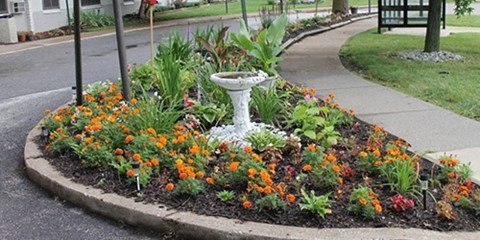 a white bird fountain in a flower garden on a sidewalk